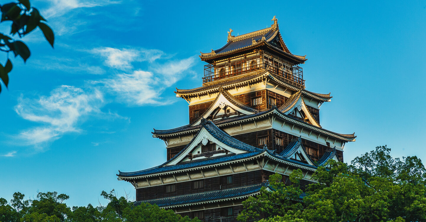 Photo: Hiroshima Castle stands amidst lush greenery and nature, lit by blue skies and the sun.