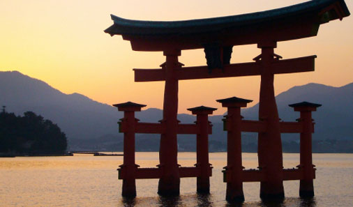 写真：緑豊かな風景を背景に、海中に立つ大きな朱色の嚴島神社大鳥居