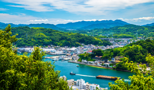 写真：山々に囲まれ、青い海には船が浮かんでいる尾道の市内