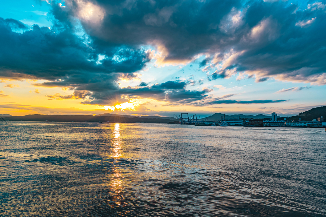 写真：雲の影から夕日が見える、夕暮れの呉湾